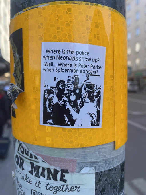 Sticker on a pole featuring a crowd and the words - Where is the police when Neonazis show up?
-Well... where is Peter Parker when Spiderman appears?