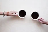 photo of 2 people's hands holding cups of coffee together 
 