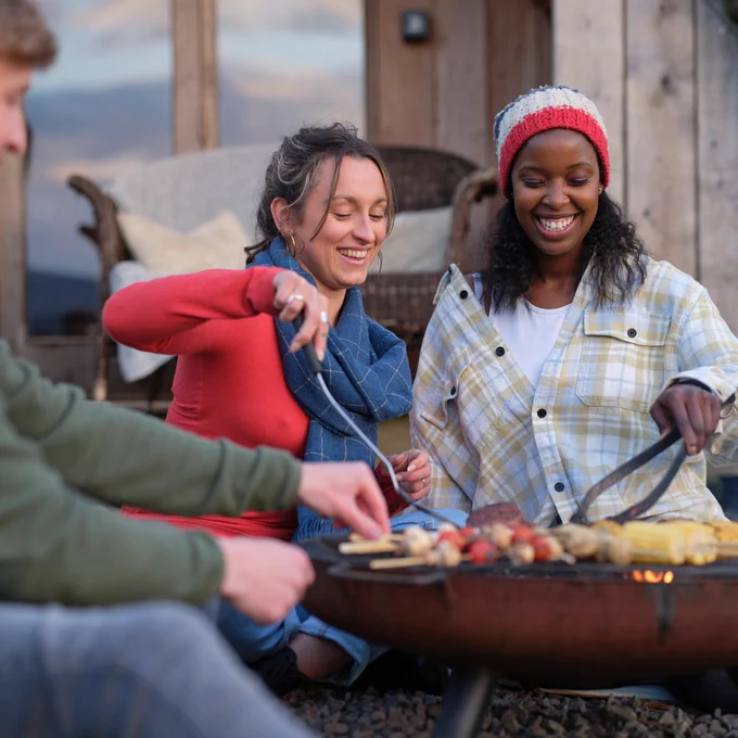 Three people sitting in front of a outdoor fire cooking food 