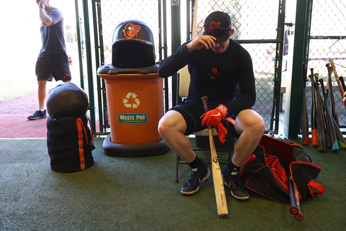 Heston Kjerstad sitting down for a break outside the batting cages with his bat resting between his legs