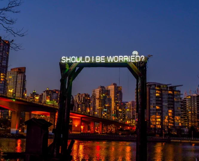 Neon sign lit up against a soft blue twilight sky along Vancouver’s seawall that reads “SHOULD I BE WORRIED?”
