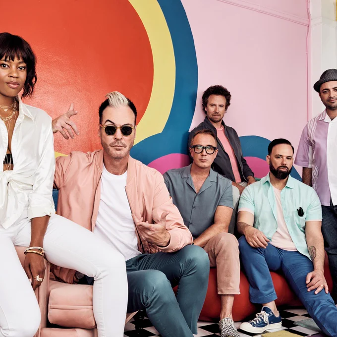 Fitz and the Tantrums band with sitting and standing in front of a colorful mural. 