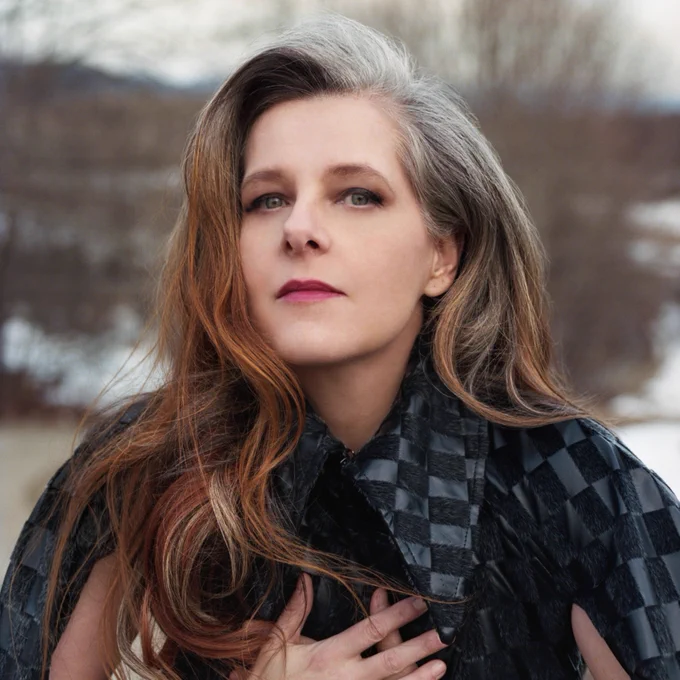 Neko Case stands outside with hands crossed at her heart. 