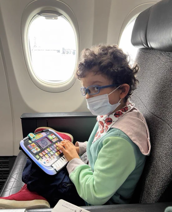 A young boy wearing a mask sitting on a plane holding a toy.