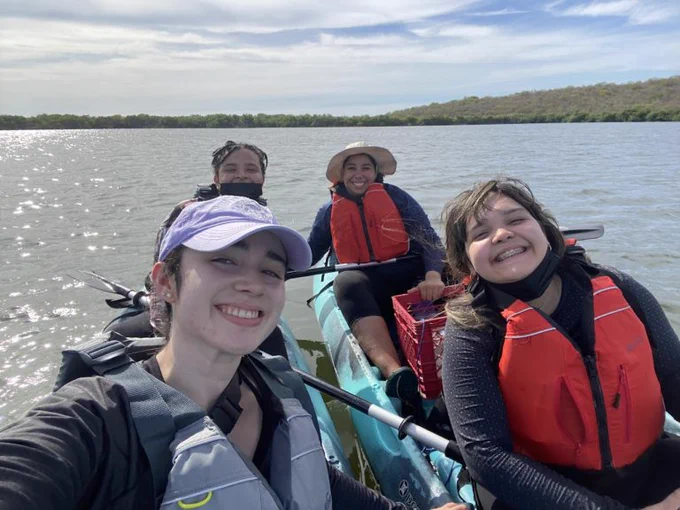 A selfie of four people sitting in two kayaks on a lake. They are all smiling and it is a sunny day with a few clouds in the sky. 