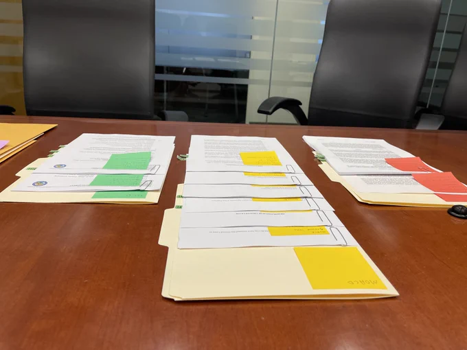 Three rows of folders on a table with documents on top of them. The documents have sticky notes on them.