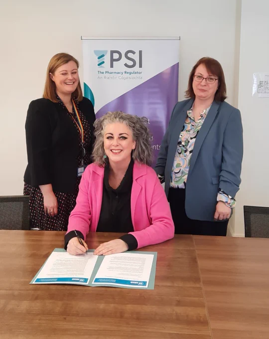 President of the PSI Council, Ms. Muireann Ní Shúilleabháin (seated), watched by Ms. Joanne Kissane, PSI Registrar (left), and Ms. Geraldine Campbell, PSI Audit & Risk Committee Chair (right), as Ms. Ní Shúilleabháin signs the Integrity at Work Pledge on behalf of the PSI, the pharmacy regulator. 
