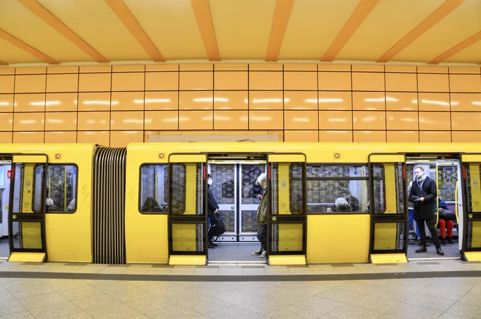 A bright yellow U-Bahn passenger train waits at the platform with doors open at a station in Berlin.