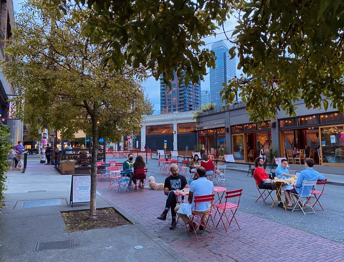 People sitting together at small cafe tables talking on a street. some trees, some nearby commercial buildings, and a sign that says Mammon streeterie in the background with said outdoor dining cafe. A few people sitting outside have dogs.

Qagggy says: During pandemic, we caught a glimpse of what Melrose could have been...a beautiful space full of people (and one or two dogs).
 https://twitter.com/Qagggy/status/1631917325824950273