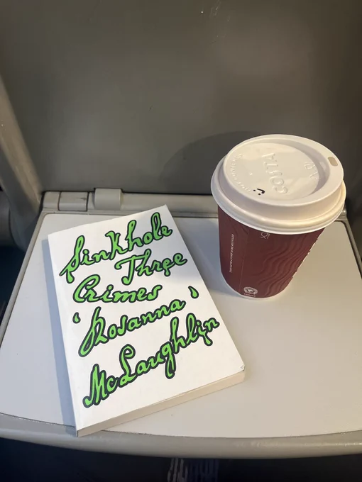 A fold down train tray with the green slimy@book and a takeaway coffee cup