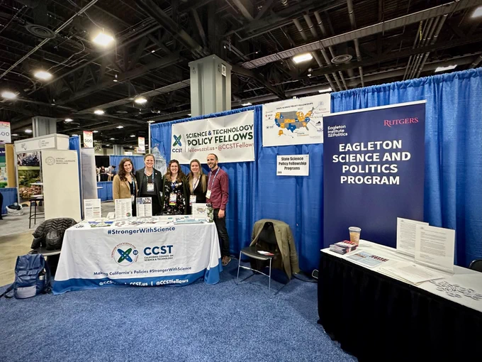 An exhibitor booth with people standing behind a table with banners and swag.