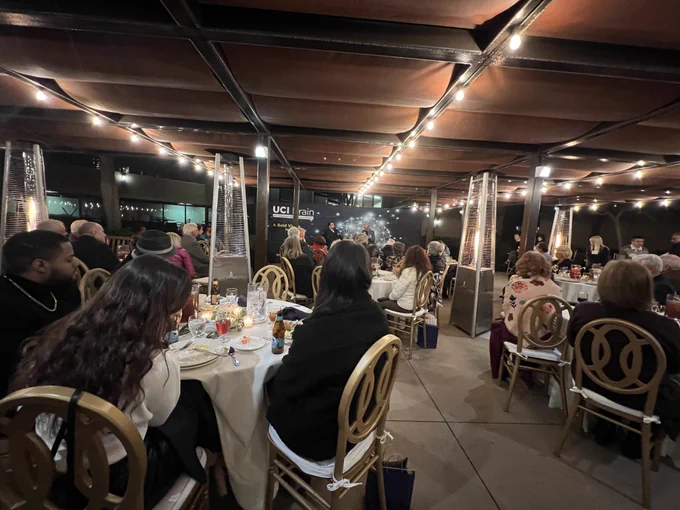 Photo of event guests sitting at round tables eating dinner and listening to Mike Yassa and Julian Thayer. Event took place in the courtyard of the CNLM. Outdoor string lights light up the courtyard.