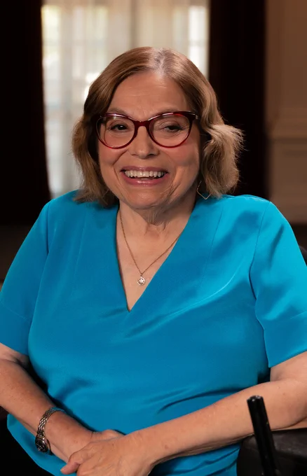 Judy Heumann, legendary disability rights advocate, is shown wearing a blue blouse and smiling.