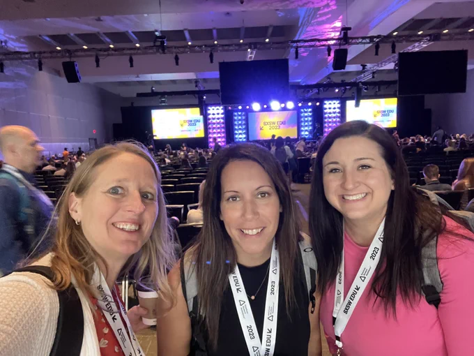 Noelle, Sara, and Carolyn smiling in front of an auditorium with screens at SXSW