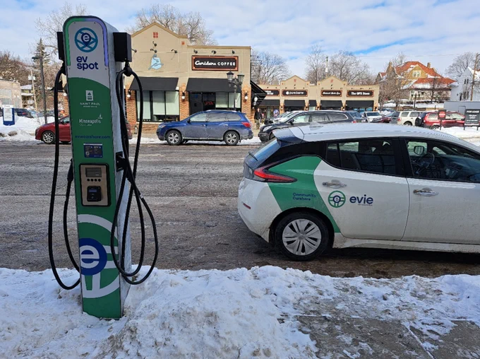 Image of Evie Carshare Electric Vehicle parked in front of and electric vehicle charging station. 
