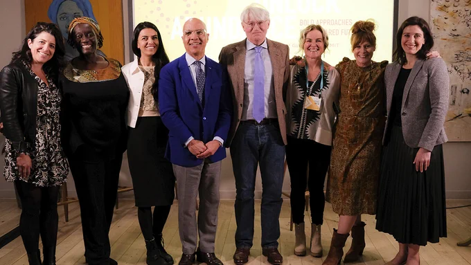 Darren Walker, wearing a blue tie and jacket, stands at the center of a group including (from left to right) Jess Houssian, Theo Sowa, Sophie Gupta, UK Development Minister Andrew Mitchell, Renee Kaplan, Jess Tomlin, and Patricia Peña