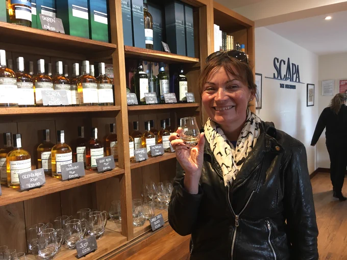 Lorraine Kelly at Scapa Distillery holding a glass of whisky in-front of a whisky display.