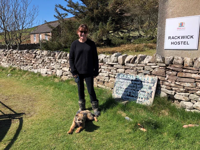Lorraine Kelly and her dog at the start of the Old Man of Hoy walk, standing in-front of the sign with safety information for climbers.