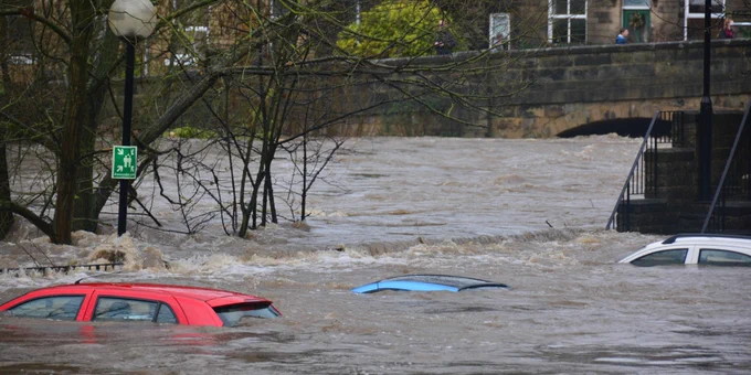 Image shows flooded road with submerged cars.
