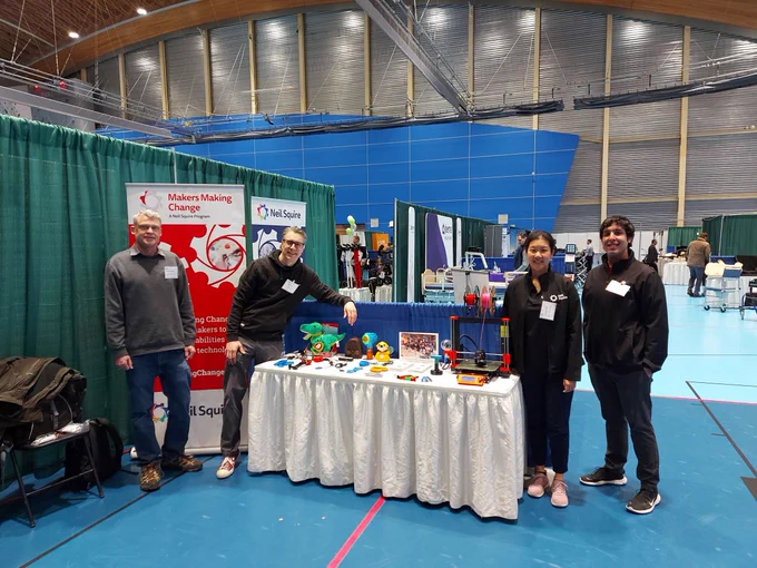 Our Makers Making Change team at a booth with a 3D printer and 3D printed assistive devices