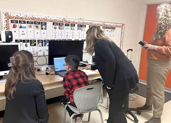 A student sitting in front of a laptop screen with 3 adults watching behind him.
