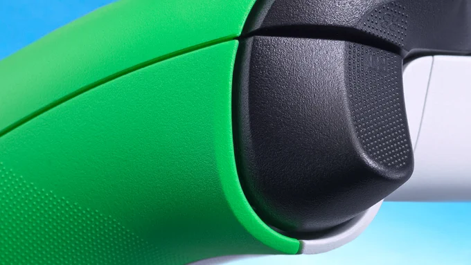 An extreme close-up of the Velocity Green Xbox controller shows the right shoulder to accentuate the black shoulder buttons and the back of the white grip against the main green of the controller, which just peeks through. Hints of the blue sky background can be seen poking out from behind the controller.