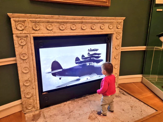 Toddler watches a video of planes in a museum gallery 