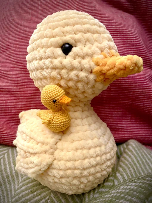 Two yellow crochet ducks showing their best (right) side. The tiny one is sitting on the wing of the giant soft squishy one.