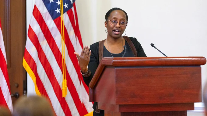 Person speaking at a podium; American flag in the background