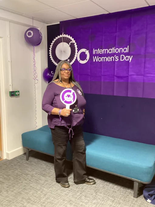 Photo of staff member holding a sign with the International Women's Day logo, the flag behind them and lanterns and balloons.
