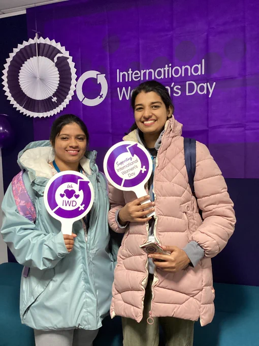 Photo of students holding a sign with the International Women's Day logo, the flag behind them and lanterns and balloons.