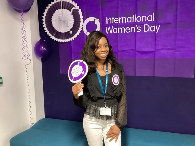 Photo of a student holding a sign with the International Women's Day logo, the flag behind them and lanterns and balloons.