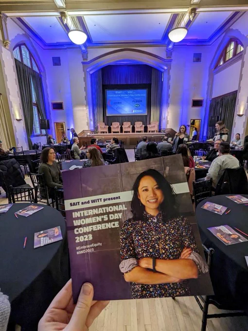 A hand is holding an event program in front of the stage where the event will take place. 
