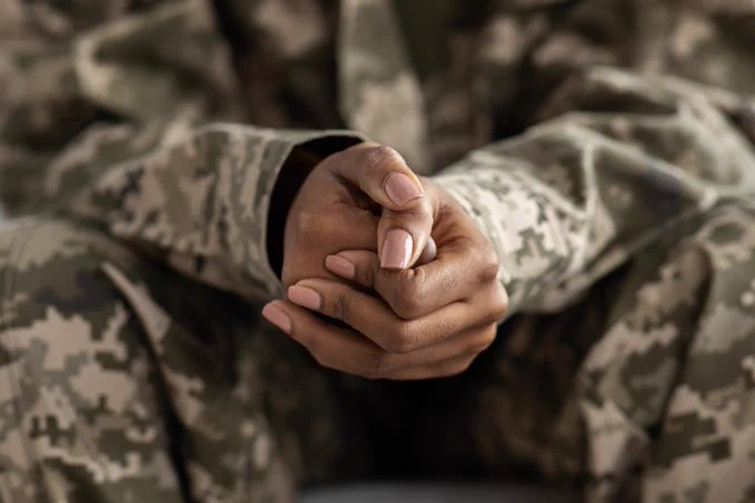 Close-up image of a Black female's hands, arms, and knees, while wearing digital-pattern fatigues. 