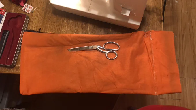 Homemade bag made of orange canvas sitting on a table w a pair of sewing scissors on top of it. You can see the zipper pull sticking out the top.