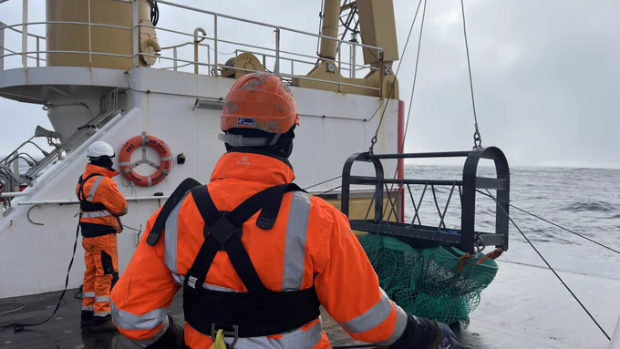 Deploying the trawl. Crew and scientists dressed in orange and attached to safety lines.