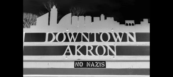 A sign featuring the skyline of Akron, Ohio and reading:
DOWNTOWN
AKRON
No Nazis