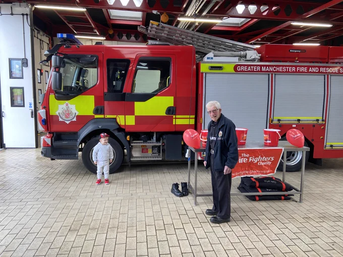 Inside the fire station with a young boy stood at the side of the fire engine and one of our volunteers with The Fire Fighters Charity donation buckets on a table with some balloons