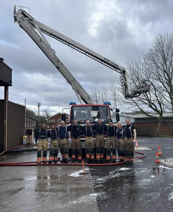 Group shot of the Fire Fighters at Oldham stood in a line in front of the fire engine after a busy day at the car wash