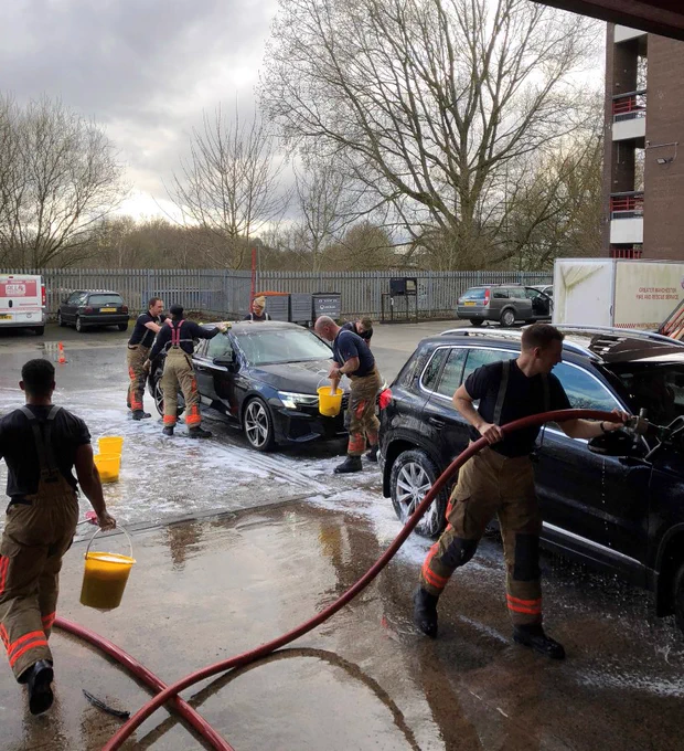 Fire Fighters busy with buckets and hoses as they clean cars in the car park