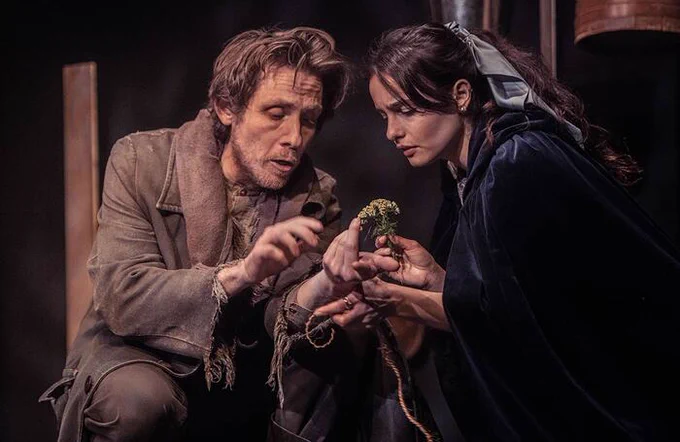 Two performers in dark brown costumes looking at something they are holding in between them 