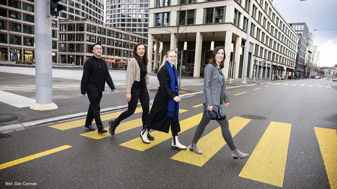 Four people walking over a crosswalk, looking to the camera.