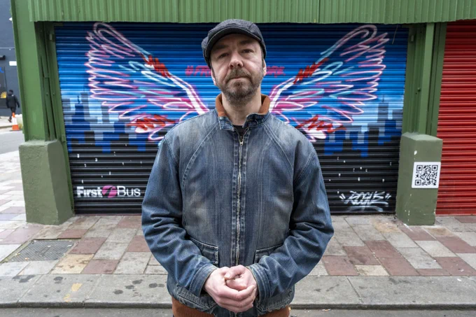 Street artist Rogue One stands in front of a garage shutter decorated with a large pair of wings.