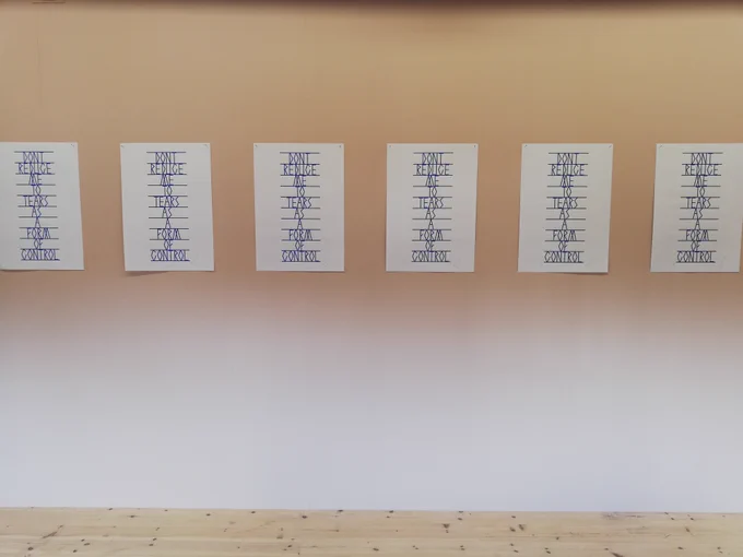 6 unframed identical prints are attached to a white wall. The print is of portrait orientation and reads 'DONT REDUCE ME TO TEARS AS A FORM OF CONTROL'. 