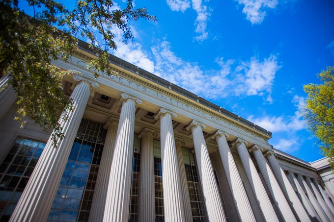 View looking up at the columns of Building 10. There is a blue sky and white clouds above.