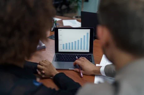 Two researchers at a large desk, looking at a bar graph of data on a laptop computer. 