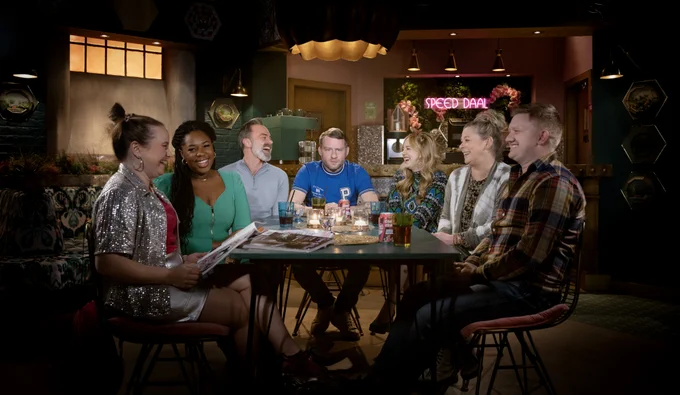 Paul, Gemma, Dee-Dee, Bill, Summer, Bernie and Chesney are sat around a table in Speed Daal. Everyone is smiling and laughing except Paul who has a worried look on his face.