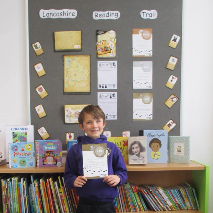 A child in the library holding their Lancashire Reading Trail certificate.