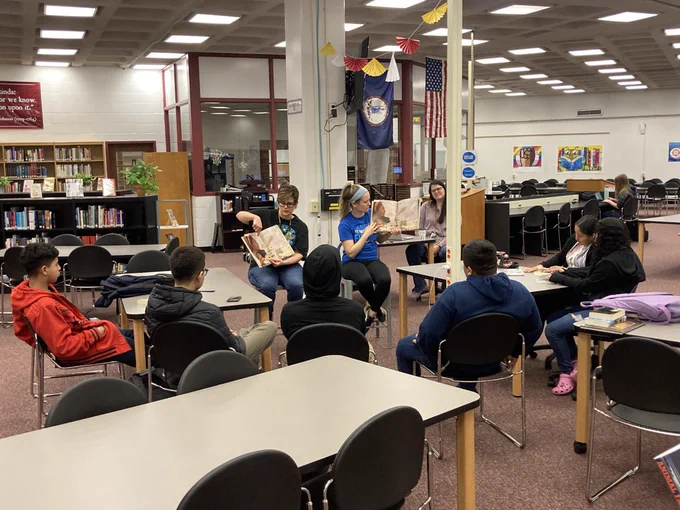 Librarians holding books and reading aloud to a semi-circle of students