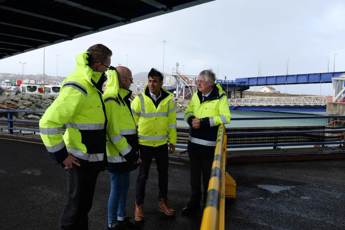 First Minister, Mark Drakeford and Prime Minister Rishi Sunak meeting with some of the Stena line staff at the port. They are all outside in the wind wearing high viz coats.